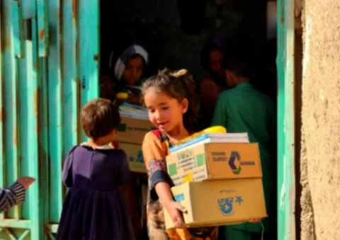 Young Afghan girl carrying aid boxes during Gate of Hope kit distribution program in Afghanistan